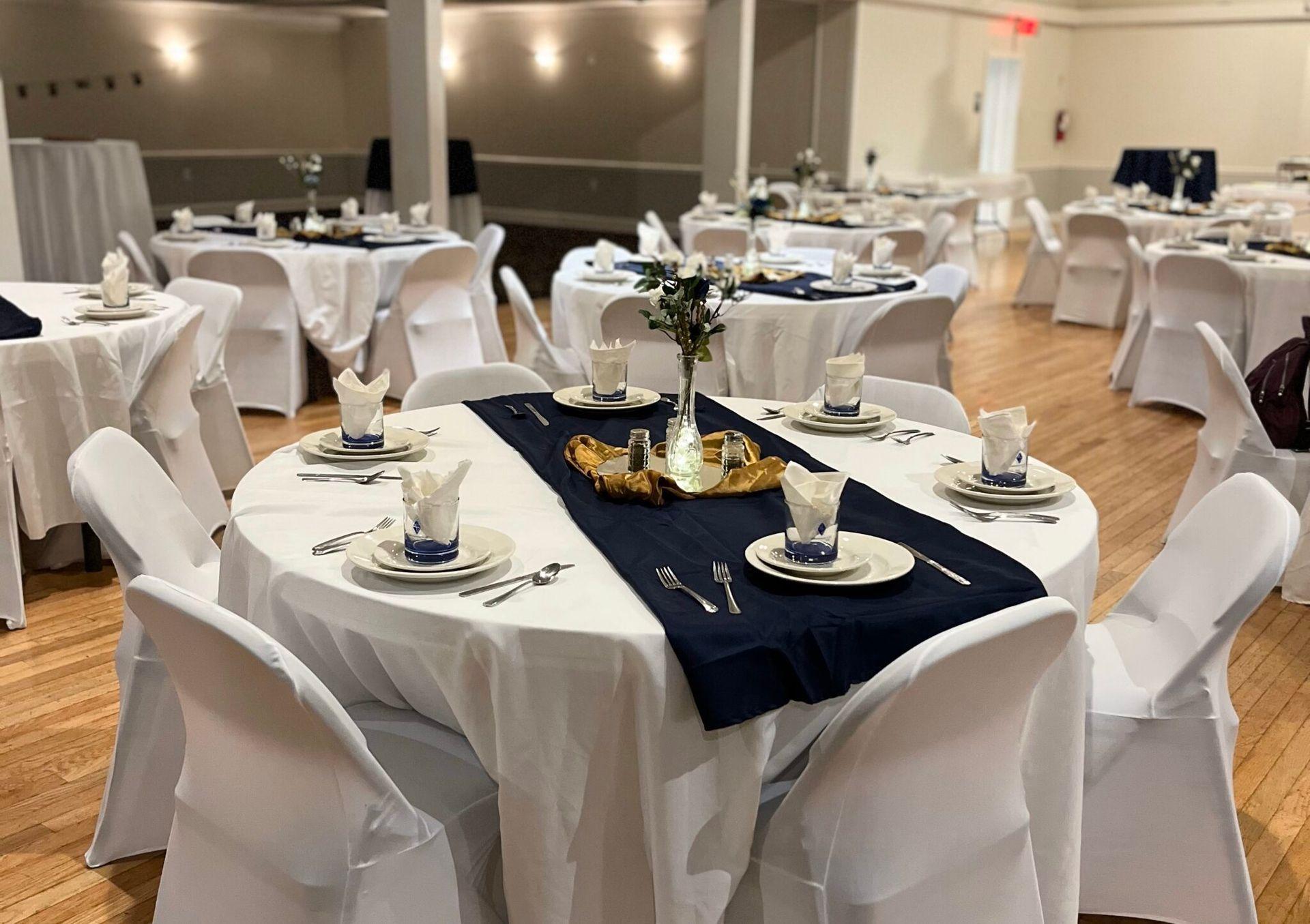 Elegant banquet hall with round tables set for an event, featuring white covers and navy blue accents.