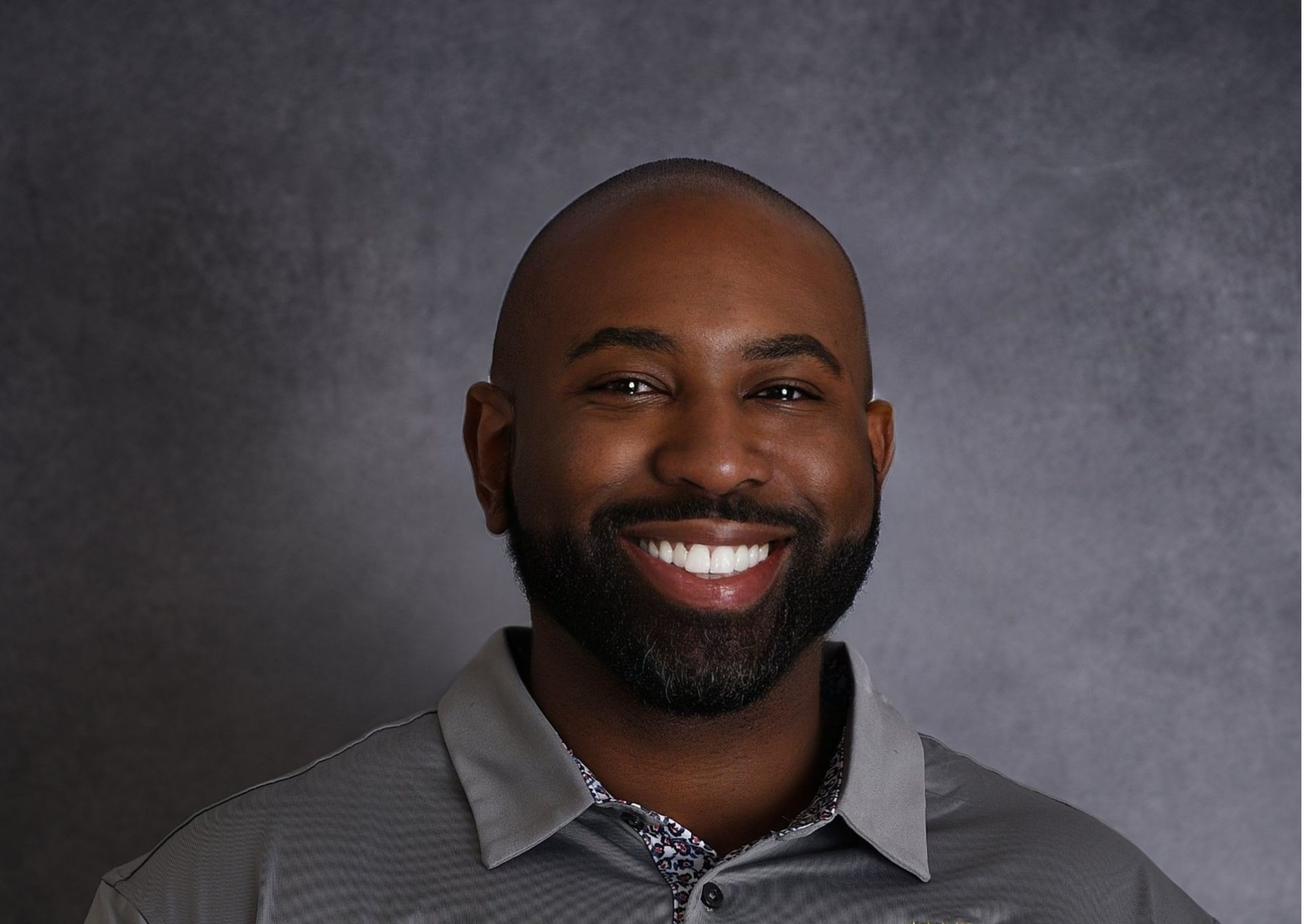 Person wearing a gray collared shirt against a gray backdrop.