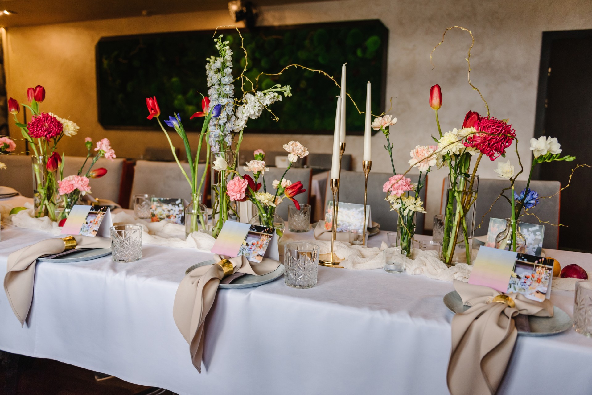 Festive dinner table is served dishes and cutlery and decorated with flowers tulips, greenery, candles. Birthday celebration. Family holidays in modern restaurant. Stylish spring party. Wedding event.